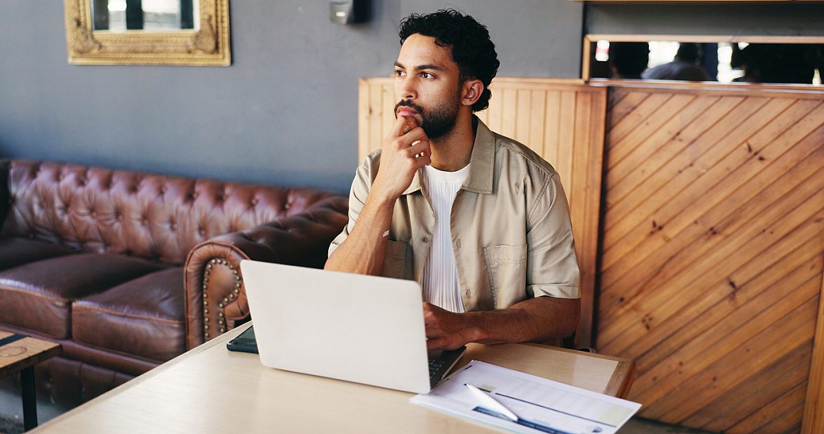 Documents, thinking and man on laptop in cafe for finance review, budget planning and research. Coffee shop, remote work and person on computer with paperwork, graph and charts for financial analysis
