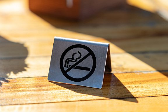 No smoking sign on a wooden bistro table outside in the sunlight